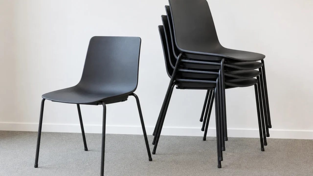 Pile de chaises de bureau à châssis tubulaire, avec une chaise identique posée seule à côté.