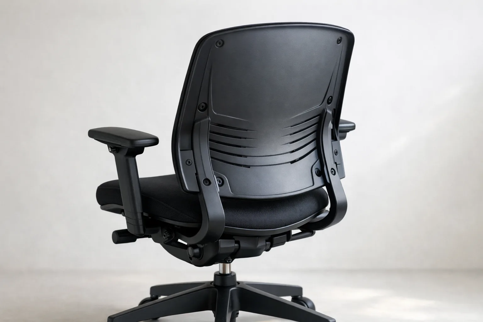 Dossier incurvé en plastique moulé d’une chaise de bureau, avec ses nervures et ses fixations visibles.