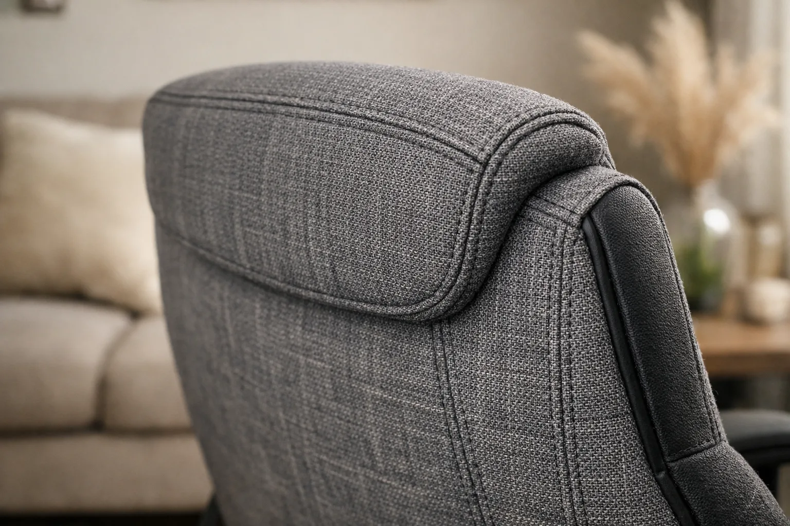 Détail du tissu et des coutures d’un fauteuil de bureau placé près d’un canapé.