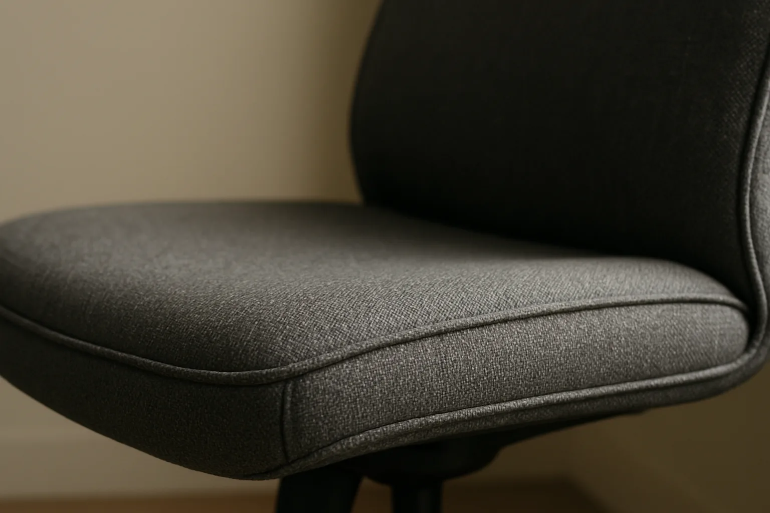 Gros plan sur le passepoil cousu au bord d’une assise de fauteuil de bureau en tissu.