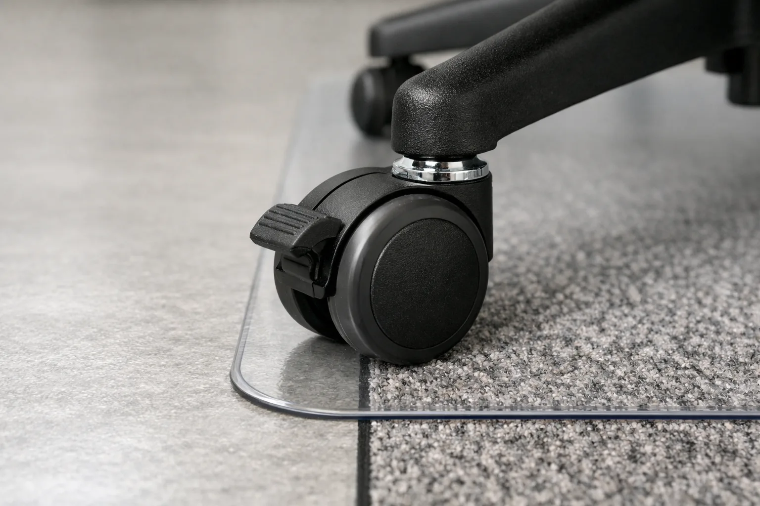 Une roulette de fauteuil de bureau posée près du bord d’un tapis de protection sur un sol dur.